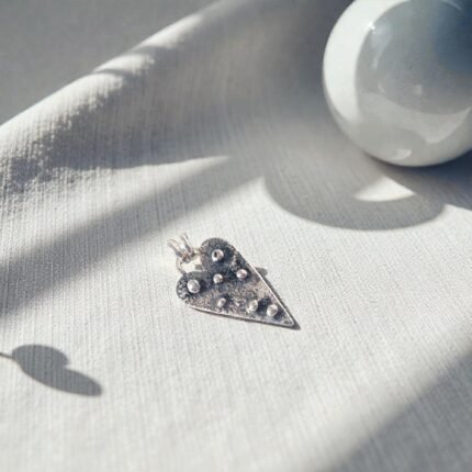 Colgante corazón de plata 950 con textura orgánica y detalles en relieve sobre tela clara