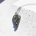 colgante Corazon con textura y pelotas de plata sobre cemento blanco - Plataia