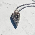 colgante Corazon con textura y pelotas de plata sobre cemento blanco - Plataia