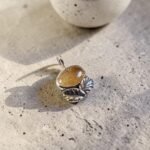 Primer plano del engaste en plata 950 con hojas talladas a mano, mostrando el tono dorado cálido de la piedra del sol
