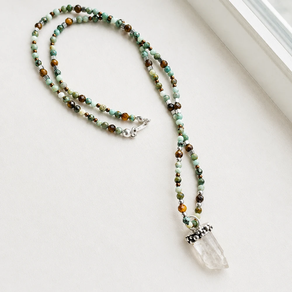 Collar-tibetano-cuarzo Collar de piedras naturales con turquesa tibetana, amazonita, ojo de tigre y bolitas de plata, con colgante de cuarzo cristal natural en bruto y engaste de plata hecho a mano.