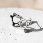 Aros pequeños de plata Círculo Balls con tres bolitas y cierre de mariposa sobre una superficie clara.